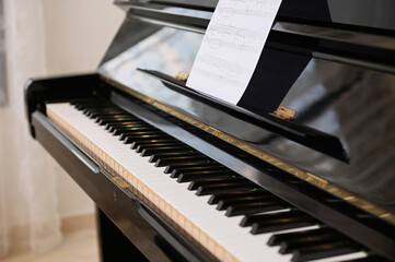 Close-up shot of old piano with open keyboard and paper sheet with notes