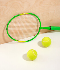 A green tennis racket and two yellow bright tennis balls on a white surface. Health and sports.
