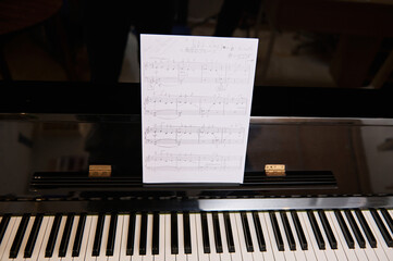 Still life of old vintage black piano with ebony and ivory keys and white paper sheet with musical...