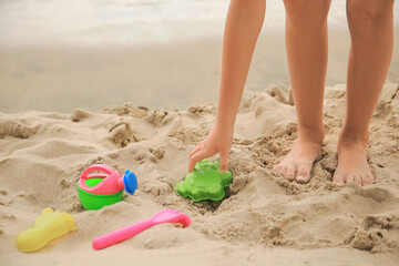 Fototapeta na wymiar Little girl playing with plastic toys on sandy beach, closeup
