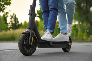 Couple riding modern electric kick scooter in park, closeup