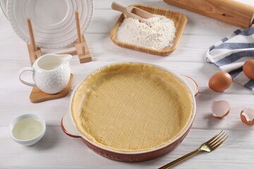 Pie tin with fresh dough and ingredients on white wooden table. Making quiche