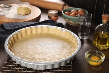 Pie tin with fresh dough and ingredients on wooden table. Making quiche