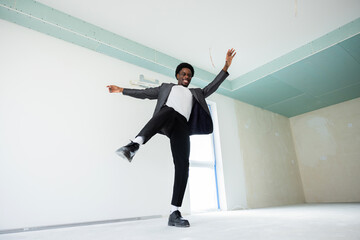 Happy african american dark skinned man wearing smart suit dancing in new just bought flat...