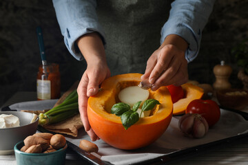 Woman stuffing pumpkin with vegetables at table, closeup