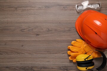 Hard hat, gloves, goggles and earmuffs on wooden table, flat lay with space for text. Safety equipment