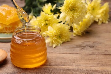 Pouring sweet golden honey from dipper into jar at wooden table, space for text