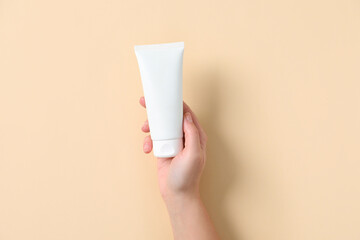 Woman with tube of hand cream on beige background, top view