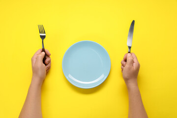 Man with fork, knife and empty plate at yellow table, top view