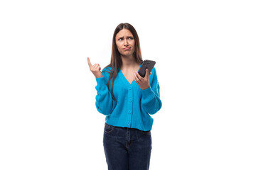 confused young brunette woman dressed in a blue sweater with buttons thinks what to answer on a message in a smartphone