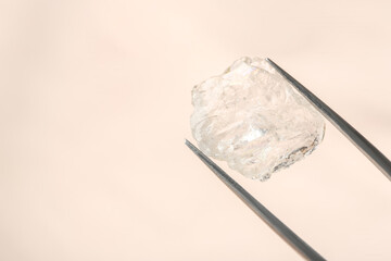 Tweezers with shiny rough diamond on beige background, closeup
