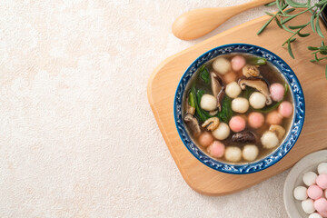 Eating homemade red and white small tangyuan with savory soup and vegetable.