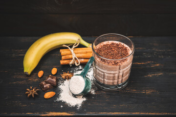 Milkshake smoothie, protein drink with grated chocolate in a glass on dark wooden board with...