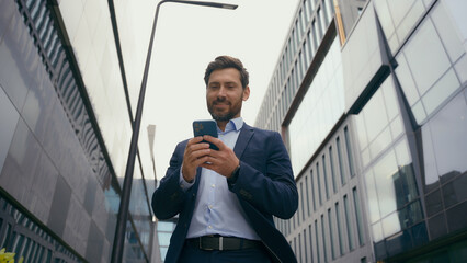 Caucasian middle-aged positive businessman in city male entrepreneur employer man business browsing chatting smartphone web distant communication connection looking away message with mobile phone