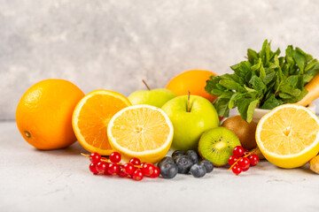 Oranges, apples, lemons, kiwi, mint, red currants and blueberries on a textured cement background. Fruits and berries. Vitamins for immunity. Place for text. Copy space.