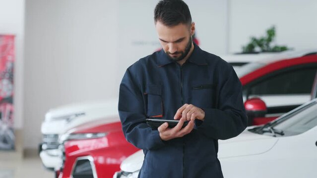Automotive mechanic running diagnostics software on tablet. Young vehicle service manager worker work in mechanics garage, check and maintenance to repair the engine car in workshop.