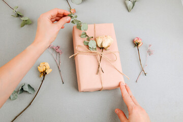Background for greetings. Gift wrapping in soft pink paper with dry eucalyptus branch on a light...