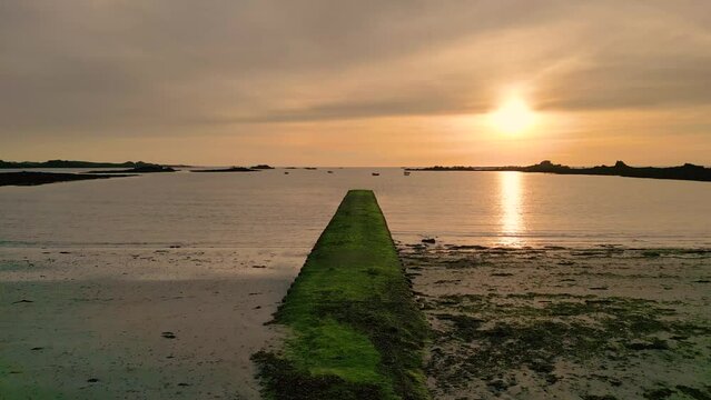 Sunset over Cobo Bay Guernsey slow flight over jetty and beach at mid tide into the sunset with boats at anchor and golden sky