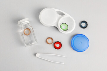 Different color contact lenses, tweezers and containers on light background, flat lay