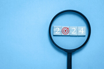 on a blue background A black magnifying glass frames a square wooden block with a target icon....