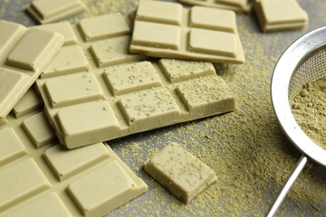 Pieces of tasty matcha chocolate bars and powder on grey table, closeup