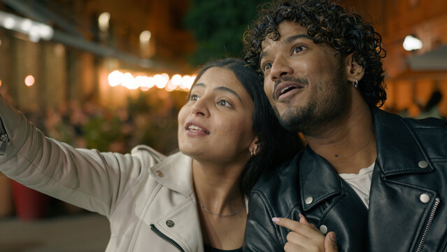 Happy laughing smiling Indian boyfriend man and Arabian girlfriend woman couple travelers tourists in new city contemplate strolling walking cuddling walk at evening night street architecture explore
