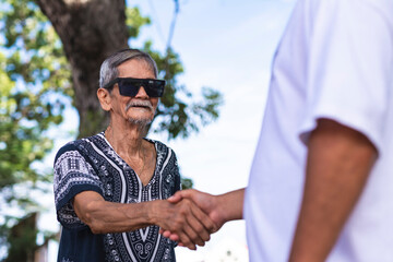 A cool hippie granddad shaking hands with a friend or his son. Wearing shades and boho style shirt....