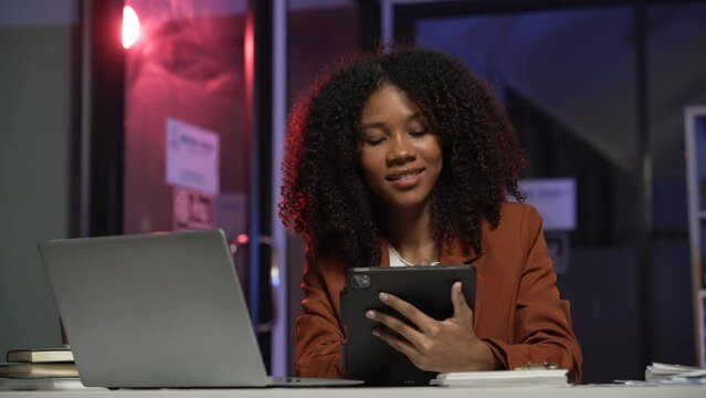 joyful African American office worker with an afro, talking on a mobile phone and writing on a notepad, with a stack of papers and a laptop on the desk.	
