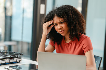 stressed African American woman with an afro hairstyle, looking at a laptop with a hand on her...