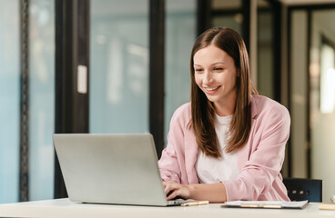 smiling Caucasian university student at a desk with a laptop, likely studying a subject in the...