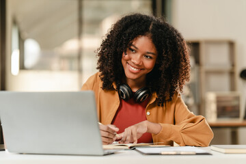 smiling African American university student with an afro hairstyle, holding a tablet and sitting at a desk with a laptop. online class learning from video conference