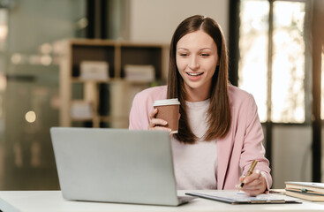 smiling Caucasian university student at a desk with a laptop, likely studying a subject in the humanities.