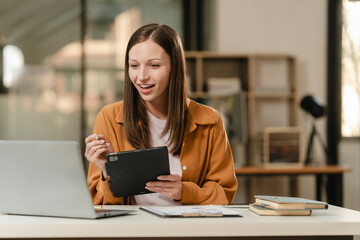 smiling Caucasian university student with a tablet, engaging in online learning, possibly studying...