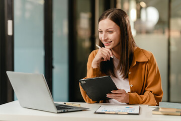 smiling Caucasian university student with a tablet, engaging in online learning, possibly studying...