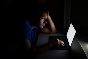 Side view of tired and stressed man working on laptop at night. Work from home concept	