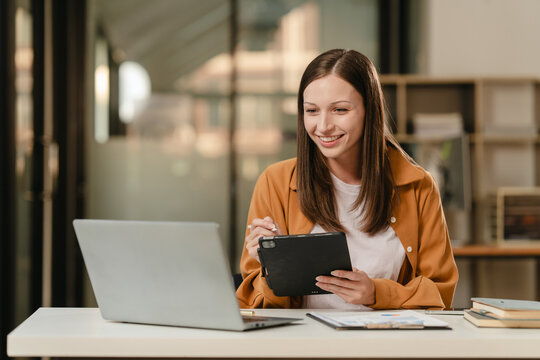 smiling Caucasian university student with a tablet, engaging in online learning, possibly studying liberal arts.