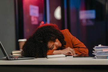 tired African-American woman with curly hair, asleep on a notebook at her desk in the office.