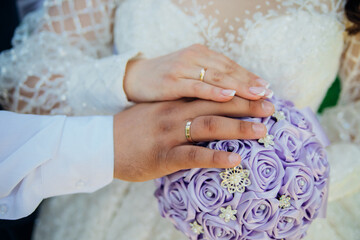 The hands of the bride and groom on a wedding bouquet made of satin ribbons. Wedding rings on the...