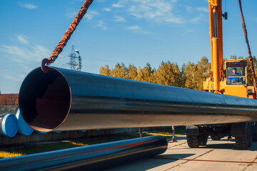 Shipment of new large diameter metal pipes on summer day from open warehouse. Tractor lift unloads pipes for gasification. Industrial background for gas equipment supplier. - obrazy, fototapety, plakaty