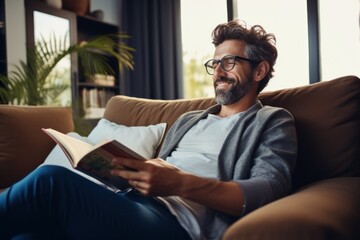 Fototapeta premium A young man relaxing at home sits on the sofa reading a book