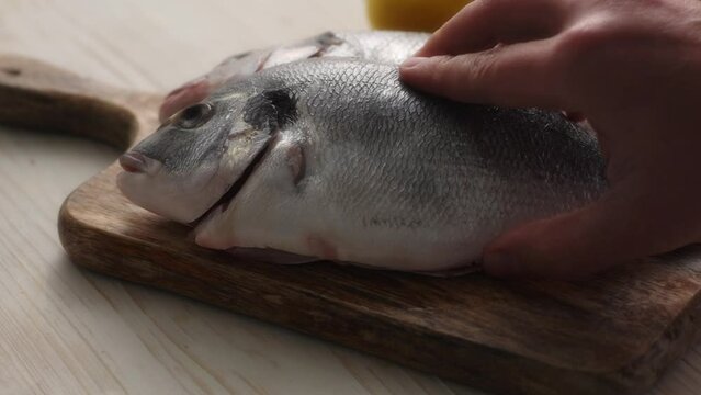 Hand puts the Gutted Fish on the Cutting Board. Close-up, shallow dof.