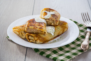 Thin fried pancakes with meat filling in a plate with sour cream and spices.