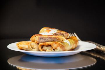 Thin fried pancakes with meat filling in a plate with sour cream and spices.