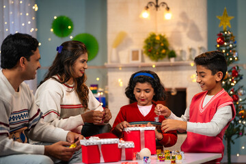 Obraz na płótnie Canvas happy Indian Sibling kids with parents preparing Christmas gifts and decorations at home - concept of festive planning, holiday celebration and family bonding