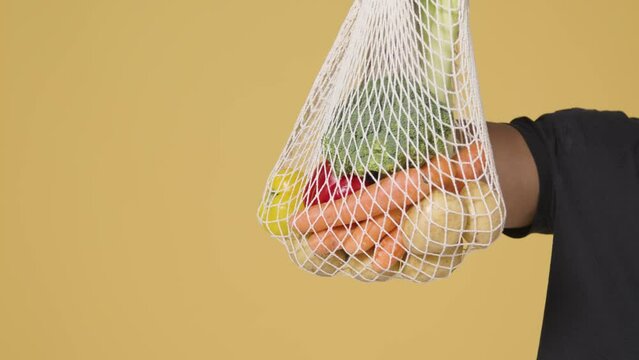 Mid Shot of Man Holding up Bag of Vegetables In Front of Yellow Background
