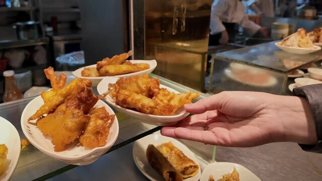 A person's hand serving a plate of crispy, fried seafood in a busy restaurant kitchen