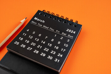 March 2024 desk calendar with pencil on orange background.