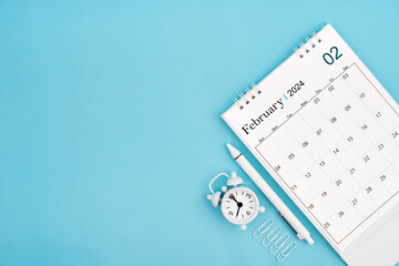 February 2024, Monthly desk calendar for 2024 year and alarm clock with paper clips on blue color...
