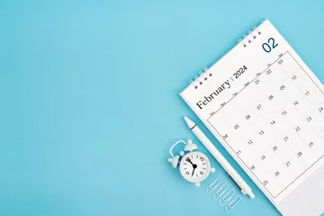 Fotobehang February 2024, Monthly desk calendar for 2024 year and alarm clock with paper clips on blue color background. © gamjai