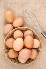 Top view of eggs in a wooden basket and egg whisk.